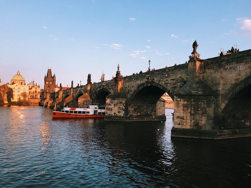Prague's Best Free Viewpoints Over Charles Bridge (No Ticket Needed) Charles Bridge towers and arches lit by sunset with tour boat