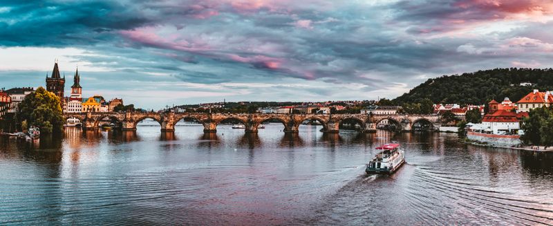 Prague's Best Free Viewpoints Over Charles Bridge (No Ticket Needed) Panoramic sunset view of Charles Bridge with passing boat