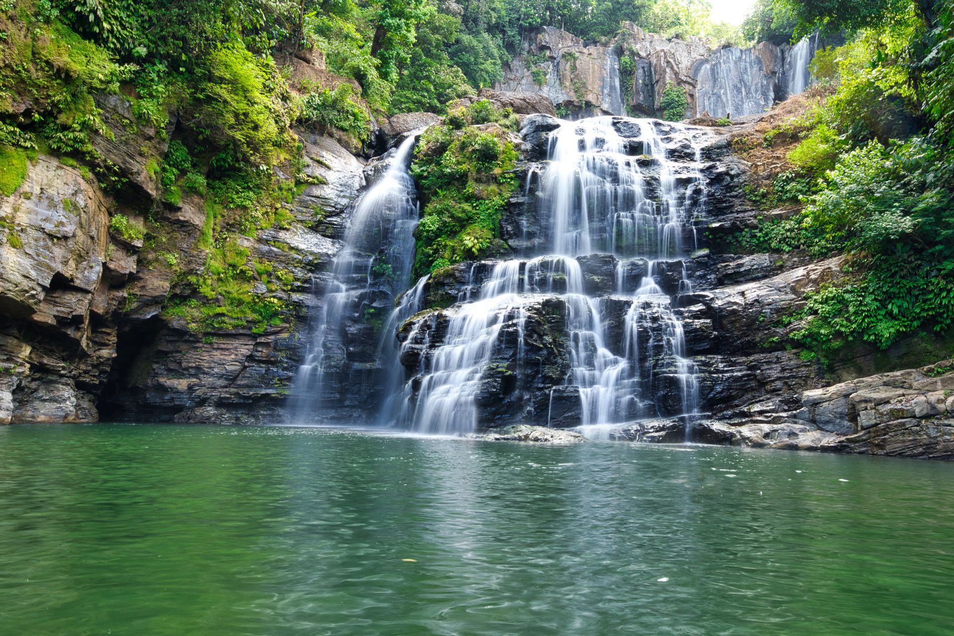 Waterfall tumbling into a calm green swimming pool