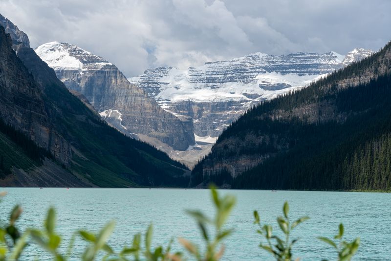 Turquoise lake with glacier peaks framed by blurred foreground leaves