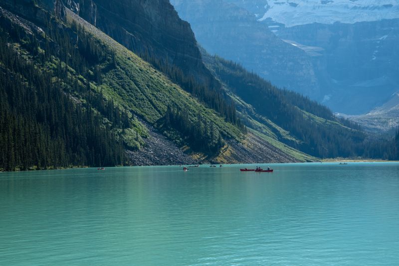 Canoes on turquoise water beneath forested mountain slope