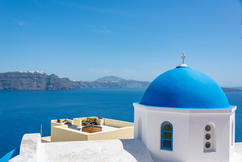 Single blue dome church with sweeping caldera sea view