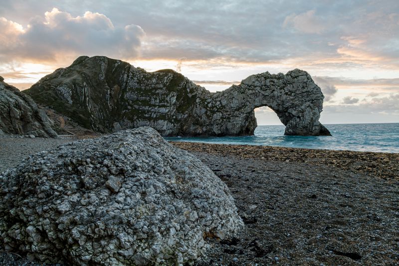 Durdle Door arch silhouetted at sunset with foreground boulder
