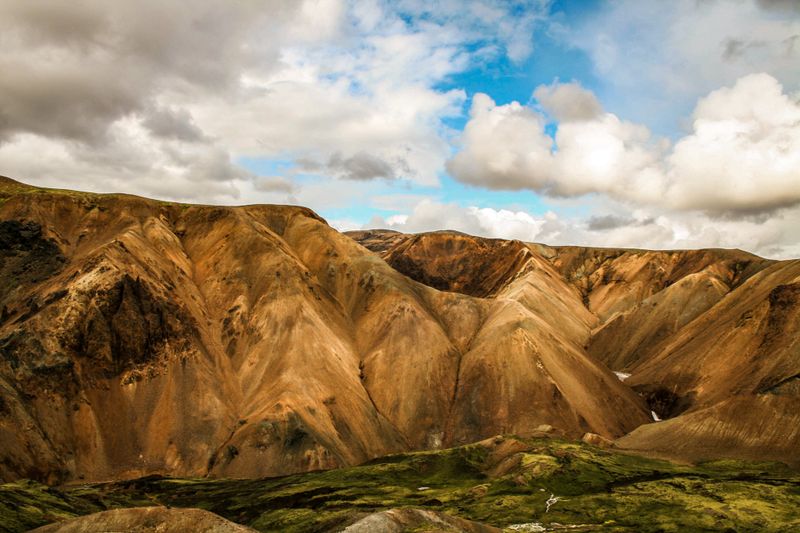 Golden striped rhyolite peaks under bright partly cloudy sky