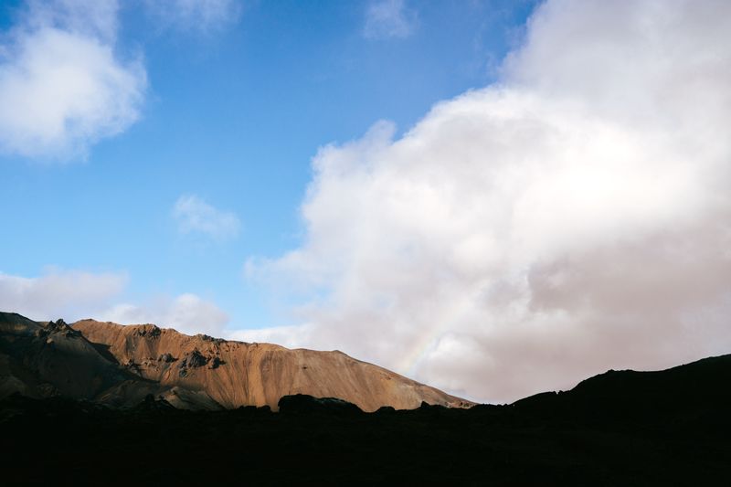 Striped volcanic ridge under blue sky with faint rainbow