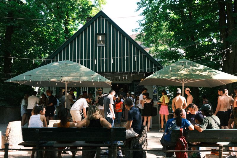 Shaded beer garden tables under trees with striped umbrellas