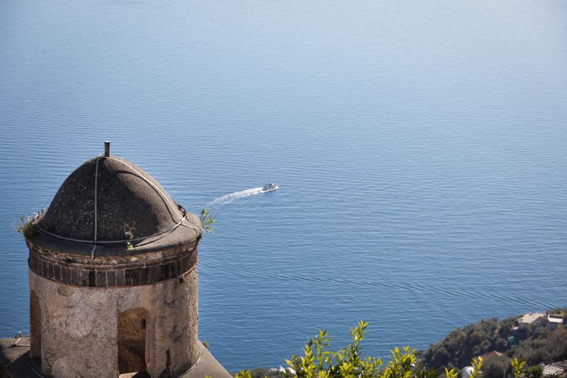 Domed stone tower overlooking blue sea with passing boat