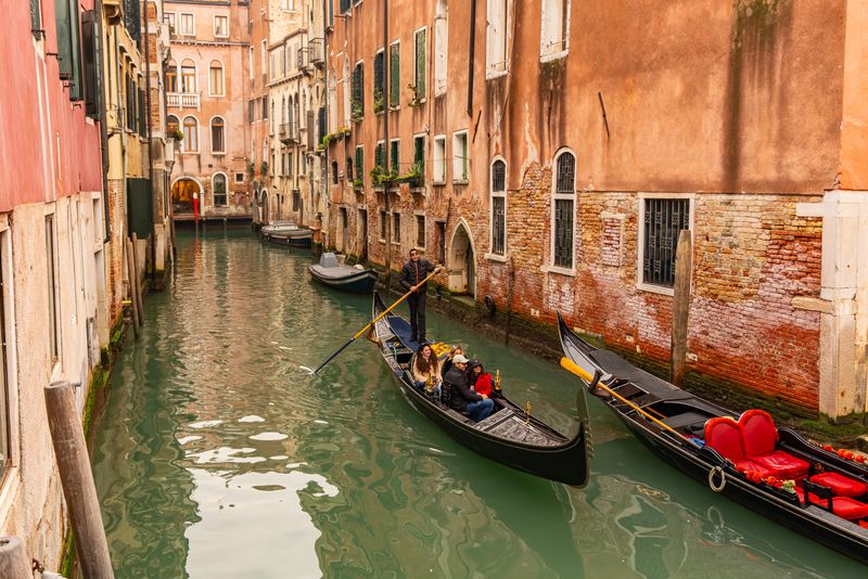 Gondola with passengers navigating a narrow shaded canal